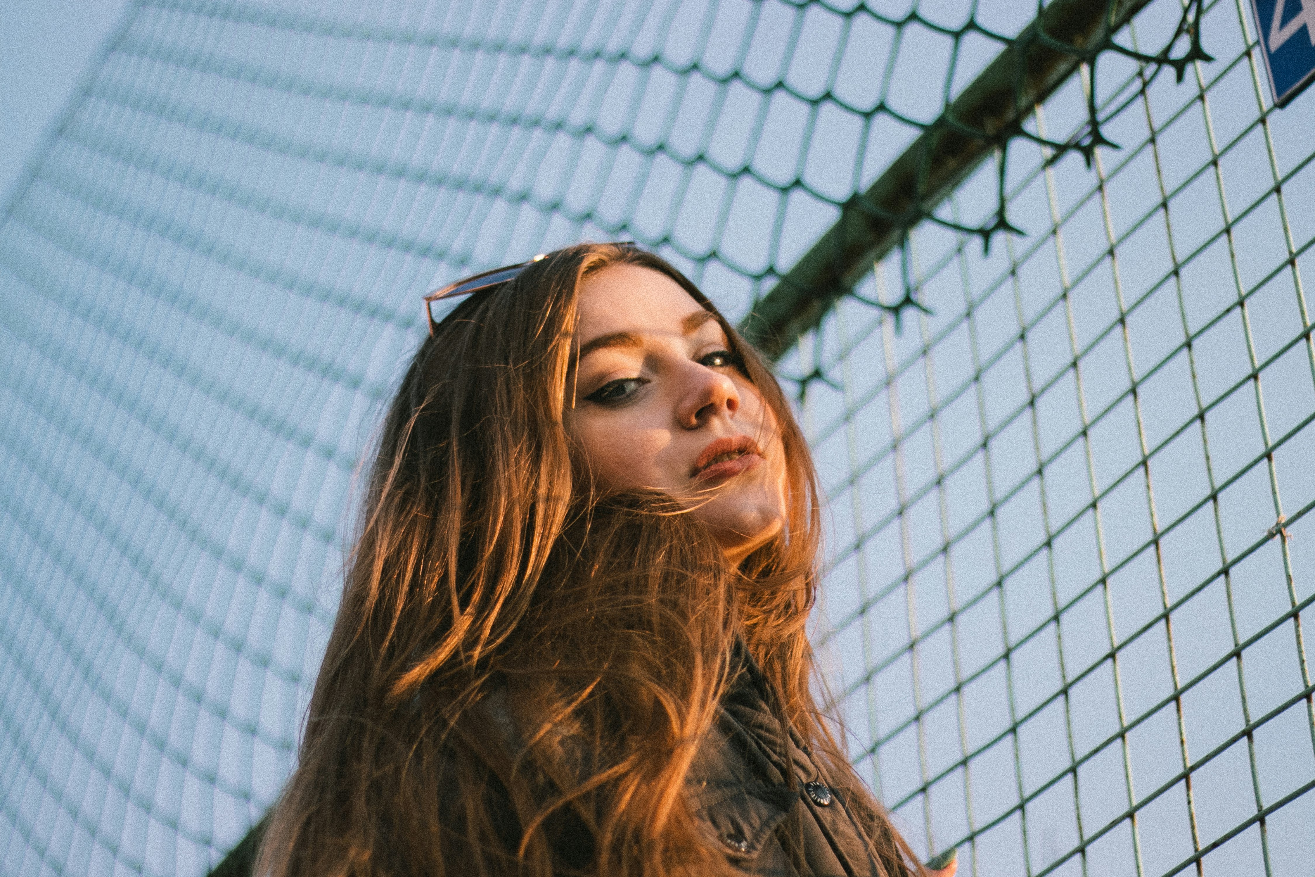 woman in black leather jacket standing beside chain link fence during daytime